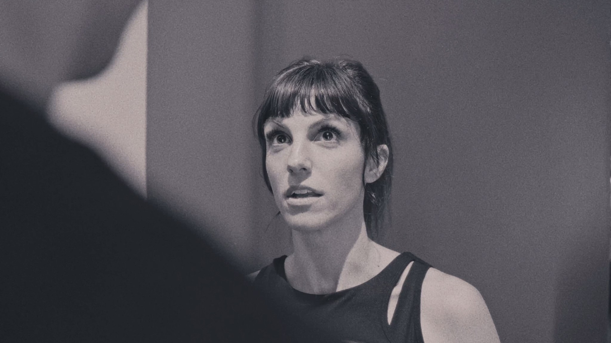 Close-up of a woman looking upward in a black-and-white interior scene.