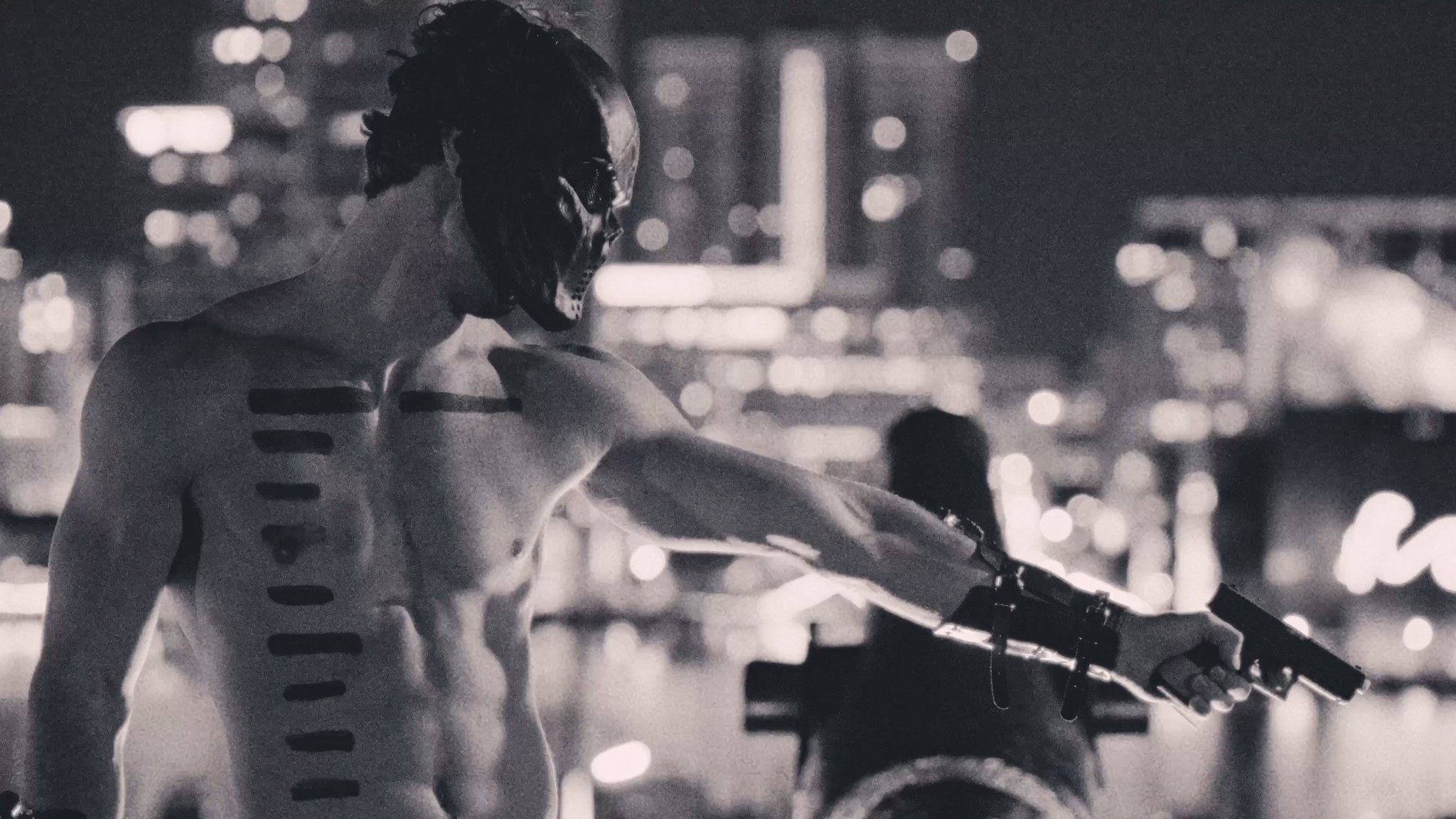 A shirtless masked man extends both arms against a blurred nighttime city background.
